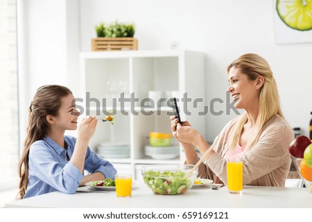 family and people concept - happy mother with smartphone having dinner and photographing her daughter at home kitchen