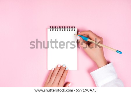 Woman's hands with perfect manicure holding pencil and spiral notepad as mockup for your design. Pink background, flat lay style. Royalty-Free Stock Photo #659190475