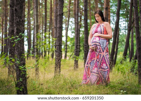 Young beautiful pregnant woman in a forest. Hands on belly. Pregnancy photography.