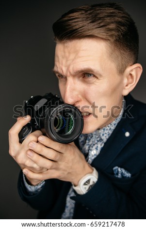 Portrait of a young photographer with a camera in his hands, with a nervous expression on his face. Studio shot