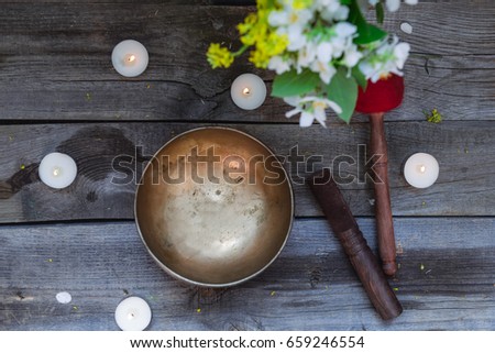 Tibetan singing bowl and special sticks, burning candles and vase with flowers on the dark wooden background, top view. Selective focus.