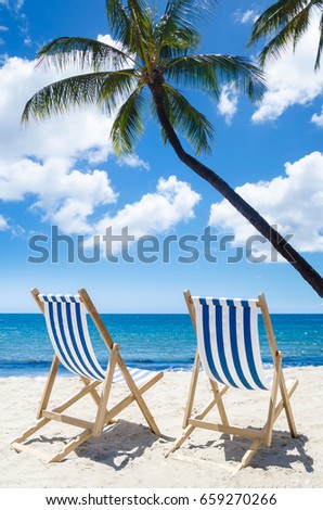 Two beach chairs under palm tree near ocean - summer background 