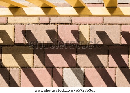 Multi-colored paving stones with a part of the fence casting a hard shadow