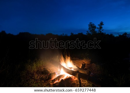 Big orange fire in bonfire at sunset with blue dark night sky