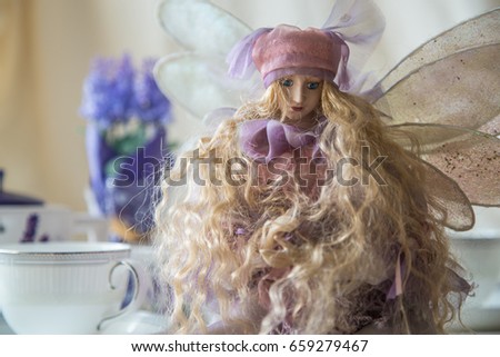 Beautiful fairy doll sitting on the table near a cup of tea, teapot and lavender bouquet