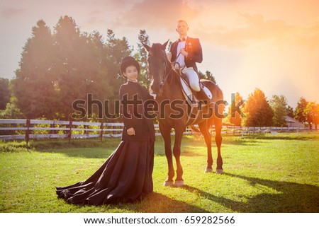 Portrait of woman standing by man sitting on horse at field during sunset