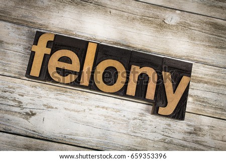 The word "felony" written in wooden letterpress type on a white washed old wooden boards background. Royalty-Free Stock Photo #659353396