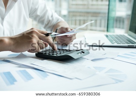 Man calculate domestic bills at home. Businessman using calculator at modern office. Young male checking balance and costs.  Start up counting finance. Business people doing paperwork for paying taxes Royalty-Free Stock Photo #659380306