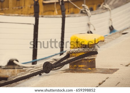 Vintage photo, Rope with old yellow mooring bollard in seaport and yacht in background, closeup and detail of yachting