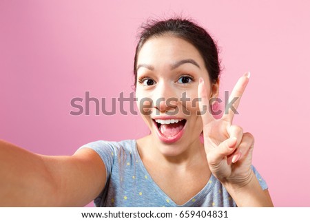 Young woman taking a selfie on a pink background
