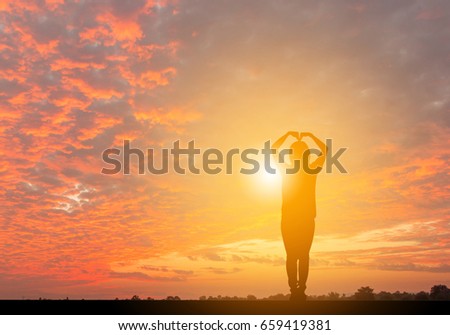 Silhouette of woman making a heart-shape symbol over beautiful sunset sky background