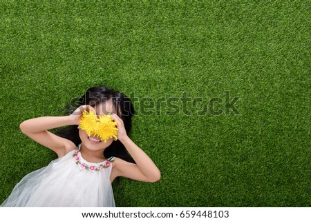 Asian Chinese little girl lying on the grass with flowers at outdoor park