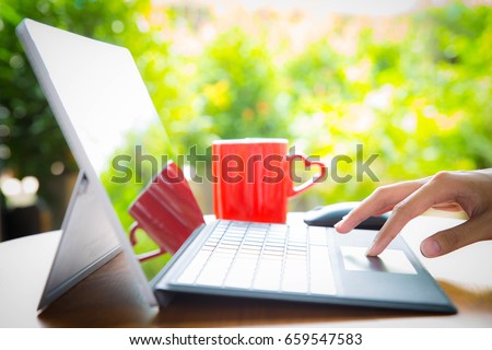 Hand of  Teenager boy touching  laptop keyboard on wooden desk with cup of coffee in the background at home , selective focus