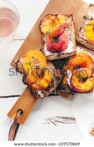 Summer snack: sandwiches with grilled peaches, cream cheese, thyme and pecan with a glass of chilled rose wine on distressed white wooden background