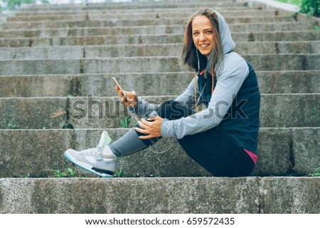 Smiling Athlete with phone relaxing on stairs in the park after workout