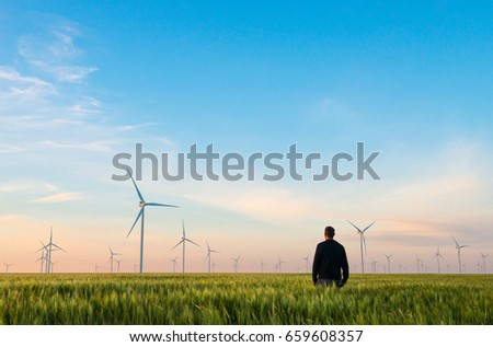 Man on green field of wheat with windmills for electric power production Royalty-Free Stock Photo #659608357