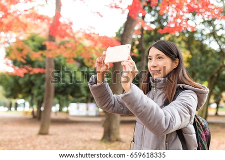 Woman taking photo in the park with maple tree