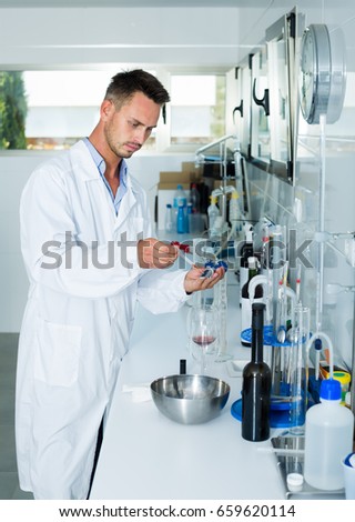 Attentive young man testing wine qualities in manufactory chemical laboratory