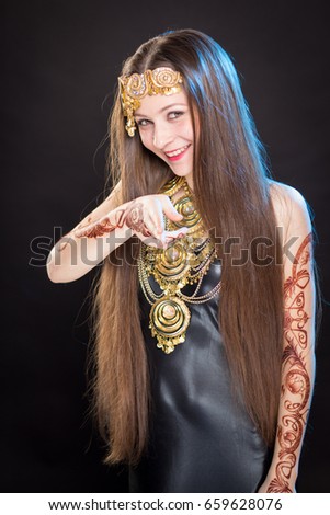 Dancer girl brunette with long hair in black suit in bronze ornaments and mehendi on hand posing and dancing on black background in studio