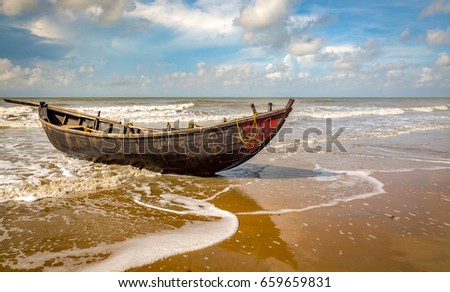 Solitary wooden fishing boat at sea beach with moody sky before sunset. Photograph taken at Taajpur beach West Bengal India.