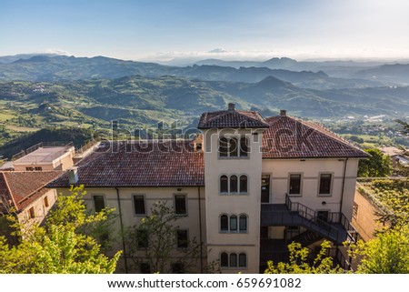 cityscape. view of one old building against a majestic mountain landscape and dramatic tender cloudy blue sky with bright sun background in San Marino, Italy, Europe
