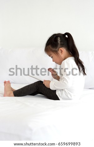 Asian little girl enjoy watching cartoon on smart tablet in bedroom