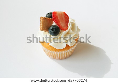Cupcake with whipped cream, fresh strawberry, blueberry and cookie on white background. Picture for a menu or a confectionery catalog.