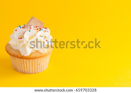 Cupcake with whipped cream, colorfull confectionery sprinkles and cookie on yellow background. The image with copy space. Background for the confectionery menu, cards, greetings, birthday invitations.