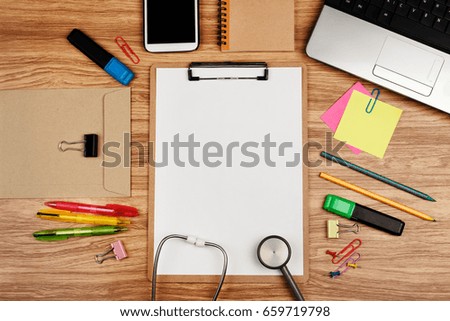 Clipboard with office supplies and stethoscope on wooden table, top view