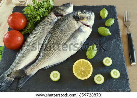 Two ready to cook raw fish with vegetables on stone slate board. Top view