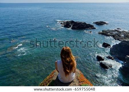 A young woman looks out over the sea from Lizards Point in Cornwall, UK