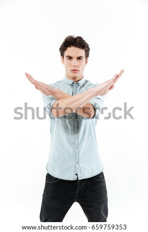 Portrait of a serious confident man standing and showing crossed arms in a no gesture isolated over white background