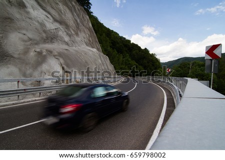 horizontal rear view of a black car with motion blur on a steep asphalt mountain road curve