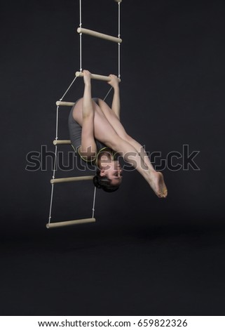 Young,smiling girl performs gymnastic exercises on a rope ladder. Studio photography against a dark background. The isolated image.