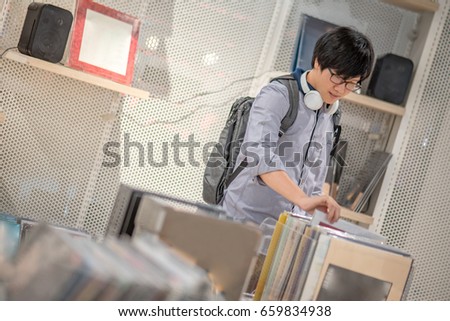 Young Asian man with headphones choosing phonograph disc in music shop, urban lifestyle concepts