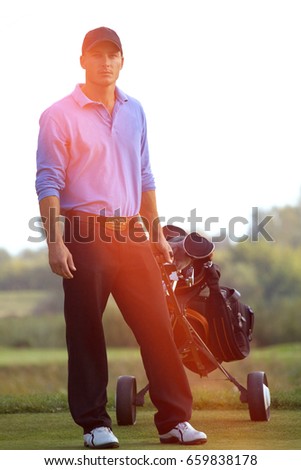 Portrait of young man carrying trolley with golf bag