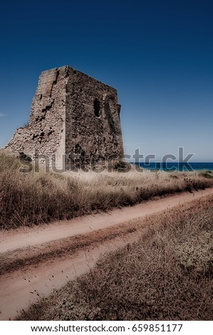 Italy June 2017 -  Stone tower with dirt road and sea in the background