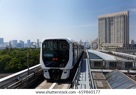Scenery of a train traveling on the elevated rail of Yurikamome Line, passing by modern high-rise buildings under blue clear sunny sky in Odaiba, Minato, Tokyo, Japan Royalty-Free Stock Photo #659860177