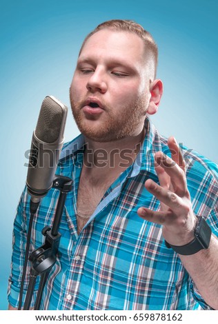 Portrait of a young showman or stand-up comic with the microphone. Blue background. Show concept.