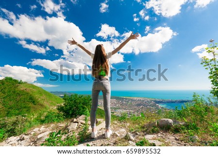 A beautiful woman goes a travel hike in holidays, has jeans, white t-shirt, slim body. Amazing summer mountains. Nature landscape. Sea in horizon. Inspiring trip. Great happy vacation .