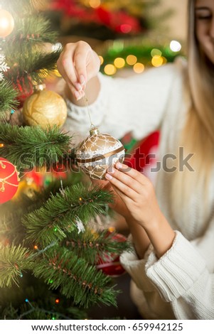 Closeup of young woman putting golden bauble on Christmas tree