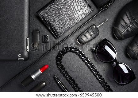 Woman accessories in business style, red lipstick, gadgets, shoes, jewelry, car key, bag, sunglasses and other luxury businesswoman attributes on leather black background, fashion industry, top view  Royalty-Free Stock Photo #659945500