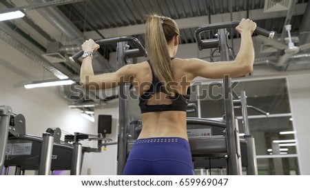 The girl pulls herself up in the gym. 