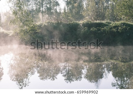 reflections in the lake water at sunrise with morning mist over the water and bright sun in summer - vintage effect look