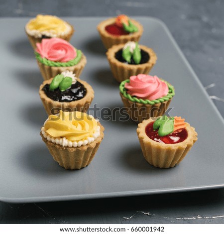 Row of colorful cupcakes on grey plate. Cakes with cream and jam on a stone background