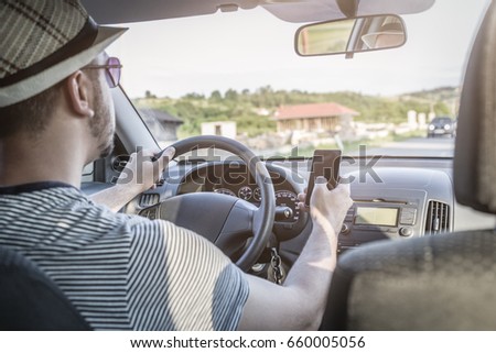 Risky behavior of young car driver. He is using cellphone while driving the vehicle. 