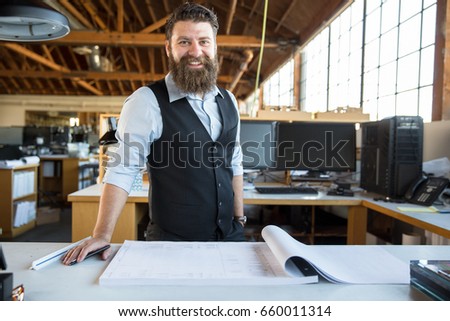 Male business owner with facial hair beard standing proudly at his work desk with paperwork 