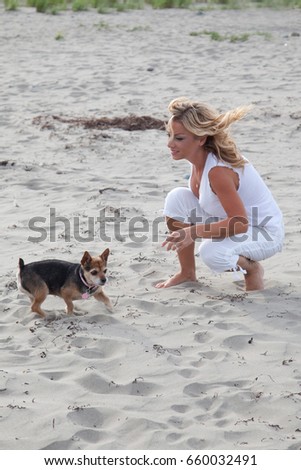 Beautiful blonde woman plays with her dog on the beach