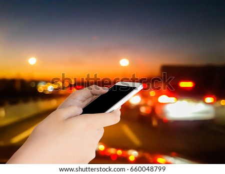 woman use mobile phone and blurred image of the traffic jam on the road in the evening with beautiful bokeh from the lights