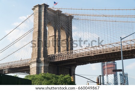 Brooklyn Bridge establishing photo of famous arch suspension cables on brick structure. America flag fly overhead during day time